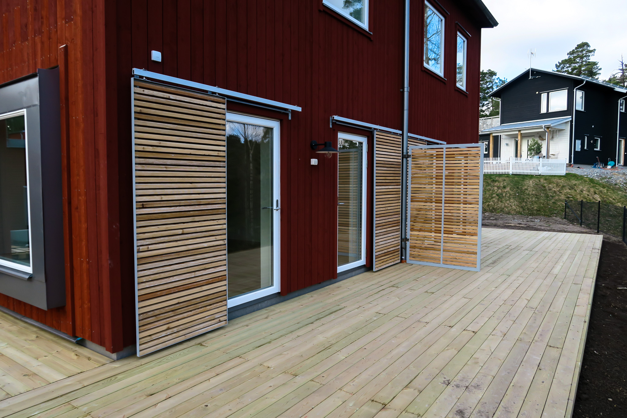 Träaltan med insynsskydd vid ett rött bostadshus